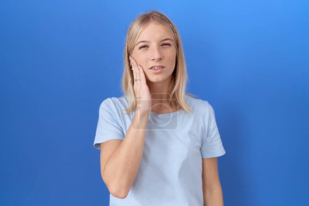 Téléchargez les photos : Jeune femme caucasienne portant un t-shirt bleu décontracté touchant la bouche avec une expression douloureuse à cause de maux de dents ou de maladies dentaires sur les dents. dentiste - en image libre de droit