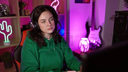 Téléchargez les photos : Une jeune femme concentrée portant des écouteurs dans une salle de jeux animée avec des néons la nuit. - en image libre de droit