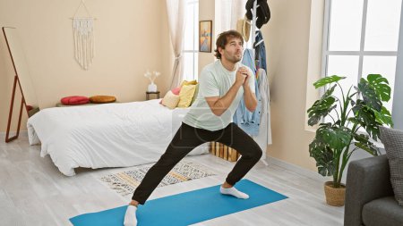 Téléchargez les photos : Un jeune homme barbu effectue un étirement de yoga dans une chambre bien décorée. - en image libre de droit