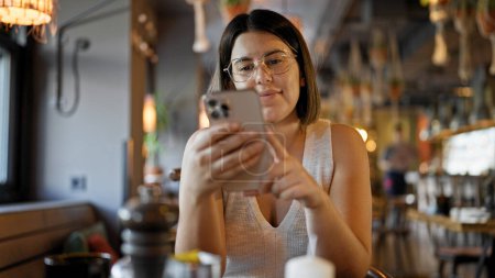 Téléchargez les photos : Jeune belle femme hispanique utilisant smartphone assis sur la table au restaurant - en image libre de droit
