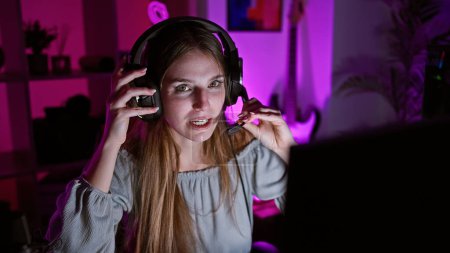 Téléchargez les photos : Jeune femme caucasienne avec casque de jeu la nuit dans une chambre éclairée rose exprime foyer et plaisir. - en image libre de droit