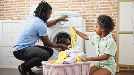 Téléchargez les photos : Afro-américain père et fille laver les vêtements à la buanderie - en image libre de droit
