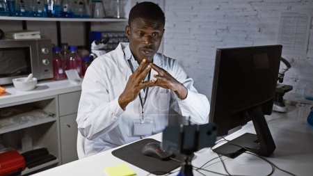 Téléchargez les photos : Un homme africain concentré en blouse de laboratoire analysant des données sur un ordinateur dans un cadre de laboratoire moderne. - en image libre de droit