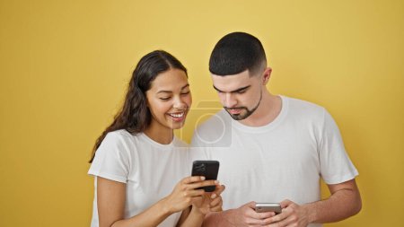 Photo for Lovely couple, caught in a beautiful moment, confidently smiling while typing on smartphones, against an isolated yellow background - Royalty Free Image