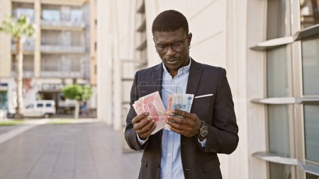 Photo for African man in business attire counts chinese yuan on an urban street. - Royalty Free Image