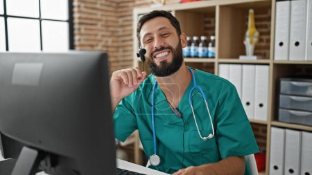 Téléchargez les photos : Jeune homme hispanique médecin faire appel vidéo avec ordinateur souriant à la clinique - en image libre de droit