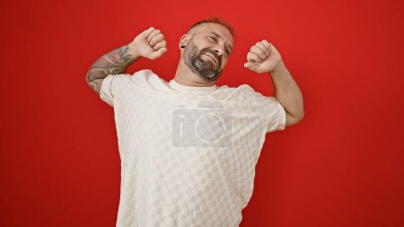 Téléchargez les photos : Jeune homme épuisé étirant les bras sur un fond rouge isolé, expression sérieuse en se tenant debout - en image libre de droit