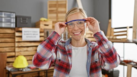 Photo for Smiling woman wearing safety glasses in a carpentry workshop - Royalty Free Image