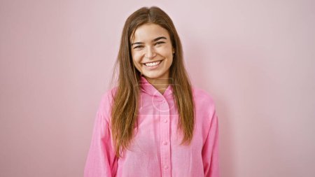 Foto de Atractiva y confiada joven hispana sonriendo alegremente sobre un fondo rosa aislado. ella está de pie casualmente, su peinado se ve fresco y lleno de alegría. - Imagen libre de derechos