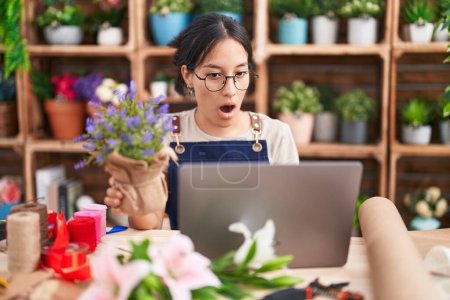 Photo for Young hispanic woman working at florist shop doing video call in shock face, looking skeptical and sarcastic, surprised with open mouth - Royalty Free Image
