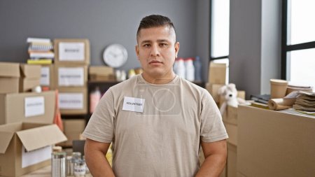 Photo for Dedicated young latin man, a steadfast volunteer standing firm, commanding serious respect in the face of charity at the heart of the community center - Royalty Free Image