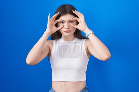 Téléchargez les photos : Young caucasian woman standing over blue background trying to open eyes with fingers, sleepy and tired for morning fatigue - en image libre de droit