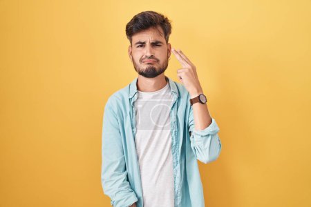 Photo for Young hispanic man with tattoos standing over yellow background shooting and killing oneself pointing hand and fingers to head like gun, suicide gesture. - Royalty Free Image