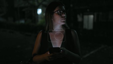 Photo for At night, beautiful hispanic woman wearing glasses holds a deep conversation over text, engrossed in her smartphone on kyoto street, amid the city's twinkling lights. - Royalty Free Image