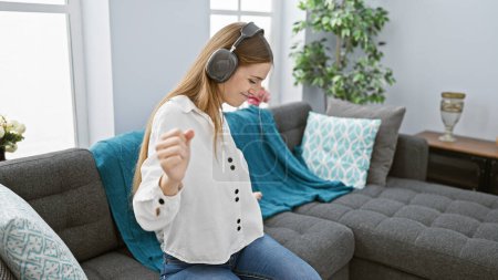 Téléchargez les photos : Une jeune femme aime danser seule à la maison avec un casque dans un cadre confortable salon - en image libre de droit