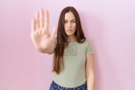 Photo for Beautiful brunette woman standing over pink background doing stop sing with palm of the hand. warning expression with negative and serious gesture on the face. - Royalty Free Image