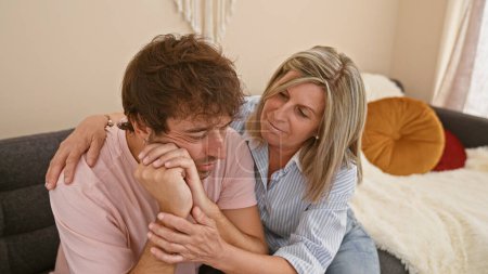 Mutter und Sohn umarmen sich unterstützend, sitzen zu Hause auf dem Sofa, Familie bewältigt gemeinsam Trauer und Angst