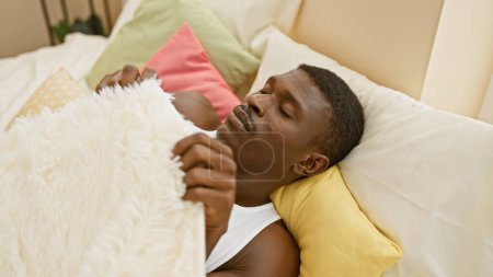 Téléchargez les photos : Un homme afro-américain dormant paisiblement dans une chambre confortable avec des oreillers colorés et des couvertures - en image libre de droit