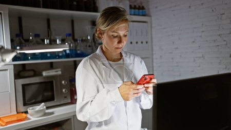 Photo for Caucasian woman scientist using smartphone in laboratory indoor setting, surrounded by lab equipment. - Royalty Free Image