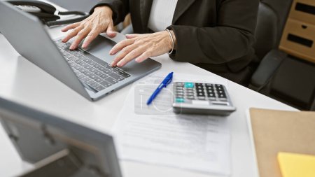Foto de Una mujer profesional trabajando en su computadora portátil en una oficina con documentos, un bolígrafo y una calculadora presentes. - Imagen libre de derechos