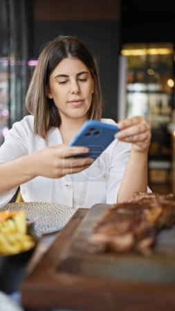 Photo for Young beautiful hispanic woman taking picture to food plate at the restaurant - Royalty Free Image