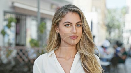 Photo for Cool, relaxed young blonde woman seriously looking at camera, standing casually in sunny urban street, attractive lifestyle portrait, outdoors with city background - Royalty Free Image