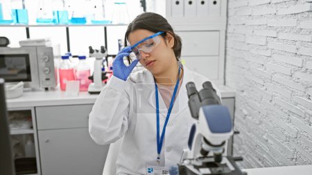 Photo for A focused hispanic woman scientist working with a microscope in a lab - Royalty Free Image