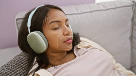 Foto de Mujer embarazada joven escuchando música relajada en el sofá en casa - Imagen libre de derechos