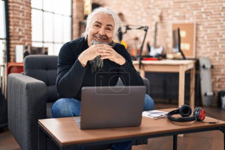 Photo for Middle age grey-haired man musician using laptop sitting on chair at music studio - Royalty Free Image