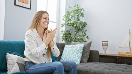 Téléchargez les photos : Jeune femme souriante se relaxant sur un canapé dans un salon moderne confortable - en image libre de droit