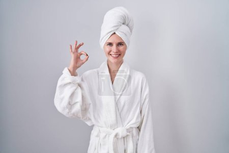 Téléchargez les photos : Blonde femme caucasienne portant peignoir souriant positif faire ok signe avec la main et les doigts. expression réussie. - en image libre de droit