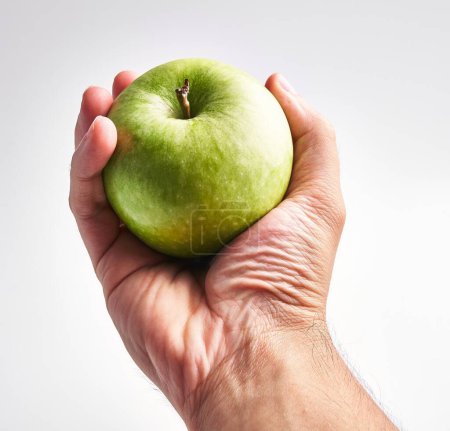Photo for A man's hand holding a fresh green apple against a white background, exemplifying health and simplicity. - Royalty Free Image