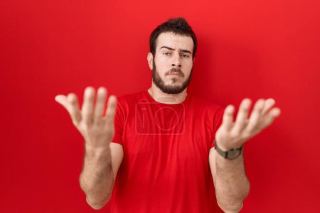 Photo for Young hispanic man wearing casual red t shirt clueless and confused with open arms, no idea concept. - Royalty Free Image