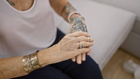 Mujer anciana que sufre de dolor de manos intenso mientras está sentada en el sofá de la sala de estar en casa, una mirada a los problemas de estilo de vida de las mujeres de mediana edad