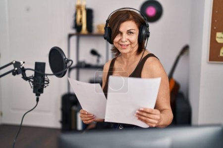 Foto de Mujer de mediana edad músico sonriendo con confianza canción de lectura en el estudio de música - Imagen libre de derechos