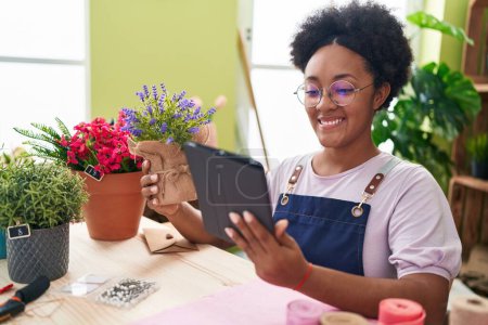 Photo for African american woman florist using touchpad holding lavender plant at flower shop - Royalty Free Image