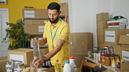 Foto de Hombre hispano joven voluntario poniendo productos en la caja de cartón en el centro de caridad - Imagen libre de derechos