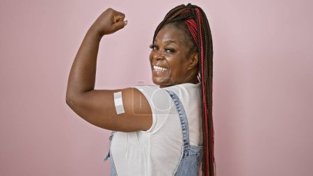 Photo for Confident african american woman, sporting braids and a band aid on her arm, exuding joy with a strong gesture. her beautiful, happy smile atop an isolated pink background, radiating positivity - Royalty Free Image