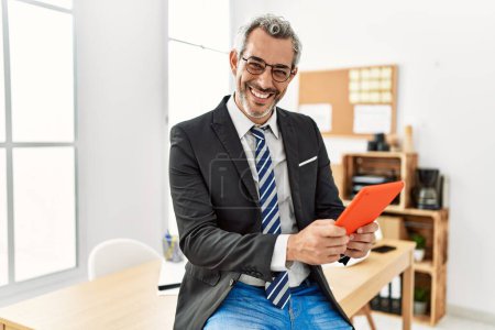 Foto de Trabajador de negocios hombre de pelo gris de mediana edad sonriendo confiado usando touchpad en la oficina - Imagen libre de derechos