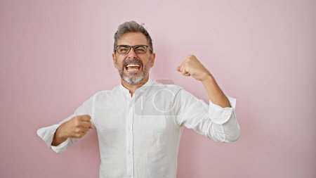 Foto de Atractivo joven hispano, canoso y con gafas, celebrando con confianza una victoria. una risa divertida y contagiosa sobre un fondo rosa aislado irradia su felicidad infecciosa. - Imagen libre de derechos