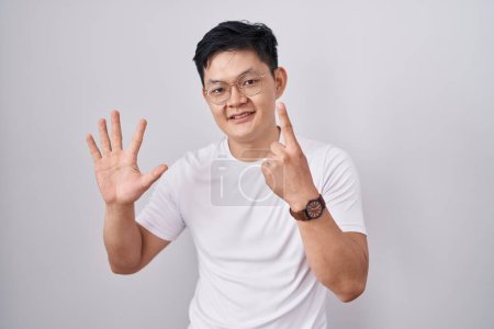 Foto de Joven asiático hombre de pie sobre blanco fondo mostrando y apuntando hacia arriba con los dedos número seis mientras sonríe confiado y feliz. - Imagen libre de derechos