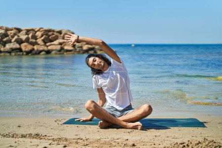 Foto de Joven hispano haciendo ejercicio de yoga sentado en la playa - Imagen libre de derechos