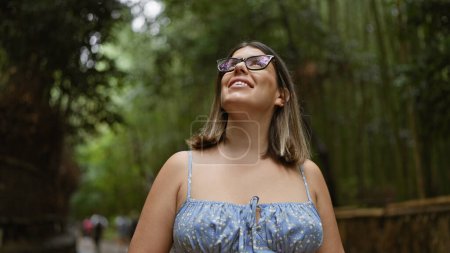 Photo for Beautiful hispanic woman with glasses, smiling confidently as she stands amongst kyoto's lush bamboo forest, looking around, full of joy and amazement. - Royalty Free Image