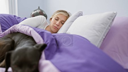 Foto de Una joven mujer caucásica y su labrador negro descansan tranquilamente juntos en un ambiente acogedor dormitorio. - Imagen libre de derechos