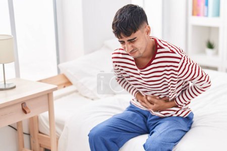 Téléchargez les photos : Young hispanic man suffering for stomach ache sitting on bed at bedroom - en image libre de droit