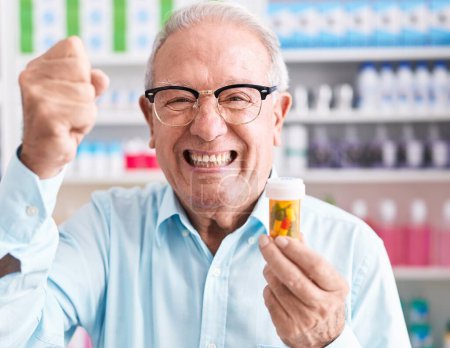 Foto de Hombre mayor con el pelo gris sosteniendo pastillas en la farmacia molesto y frustrado gritando con ira, gritando loco con la ira y la mano levantada - Imagen libre de derechos