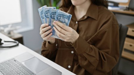 Photo for A young woman examines hungarian forint banknotes in an office setting, suggesting finance or business concepts. - Royalty Free Image
