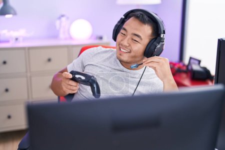 Foto de Joven hombre chino streamer jugando videojuego usando joystick en la sala de juegos - Imagen libre de derechos