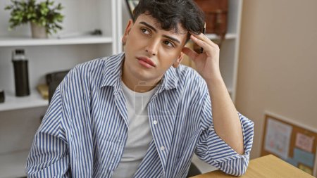 Photo for Pensive young man in office setting with striped shirt touching hair and contemplative look. - Royalty Free Image