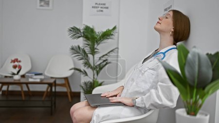 Téléchargez les photos : Jeune femme blonde médecin finir de travailler détendu sur chaise à la salle d'attente de la clinique - en image libre de droit